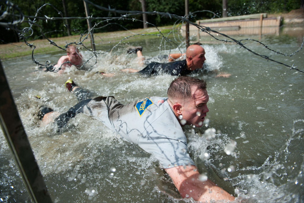 Teams in the wave of the competitors Muddy Nick 10K crawl through a water hazard, under lines of barbed-wire, during the Special Operators Challenge at the Carolina Horse Park on Saturday, May 30, 2015 in Raeford, North Carolina.